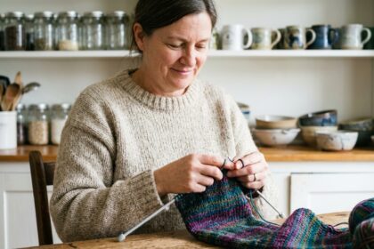 Femme tricotant une écharpe colorée dans une cuisine chaleureuse